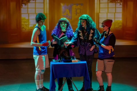 A group of four young adults standing in front of a blue table reading a book